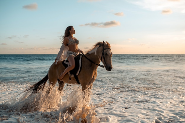 Junge Brunetteschönheit, die Spaß mit Pferd hat und auf den tropischen Strand reitet