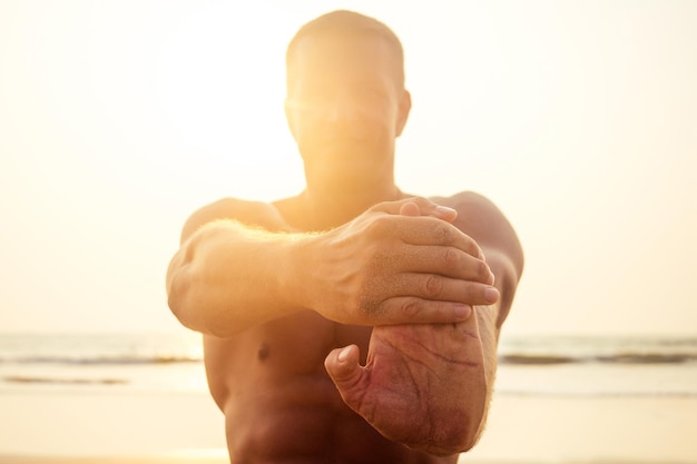 Junge brutale männliche Bodybuilder zeigt athletische Figur starken Torso bei Sonnenuntergang am Strand .sexy Boxer Trainingsübung.