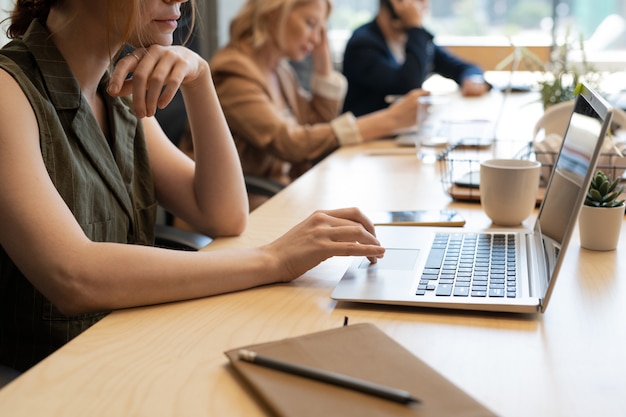 Junge Büroangestellte, die die Präsentation des Surfens im Netz vorbereitet, während sie am Schreibtisch vor dem Laptop gegen ihre Mitarbeiter sitzt