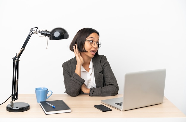 Junge Business-Mischlinge, die im Büro arbeiten und etwas hören, indem sie die Hand auf das Ohr legen?