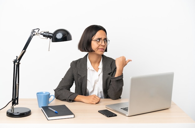 Junge Business-Mixed-Race-Frau, die im Büro arbeitet und auf die Seite zeigt, um ein Produkt zu präsentieren