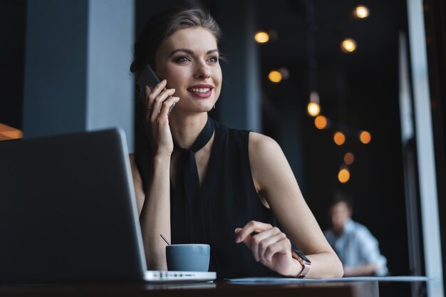 Junge charmante Frau, die mit Handy anruft, während sie in der Freizeit im Café sitzt, attraktive Frau, die während der Ruhe im Café ein Gespräch mit dem Handy führt.