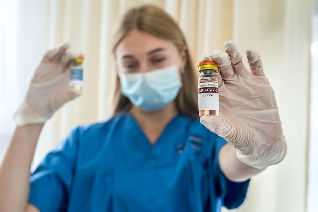 Junge charmante Krankenschwester in Handschuhen und Maske zieht einen Impfstoff mit einer Spritze zur Impfung Das Konzept der Impfung von Menschen gegen Coronavirus