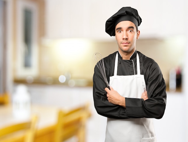 Junge Chef mit einem Kochutensilien mit einem Zweifel Geste