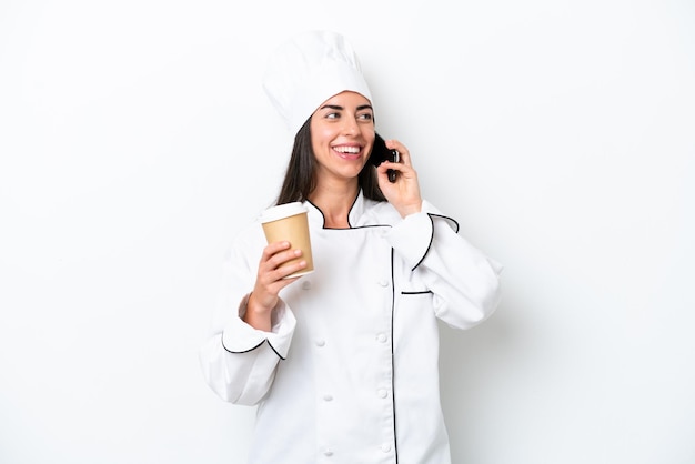 Junge Cheffrau über weißem Hintergrund, die Kaffee zum Mitnehmen und ein Handy hält