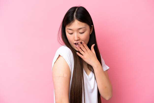 Junge Chinesin, die ein Pflaster trägt, isoliert auf rosa Hintergrund, mit überraschtem und schockiertem Gesichtsausdruck