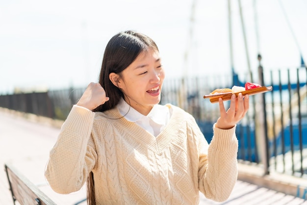 Junge Chinesin hält draußen Sashimi und feiert einen Sieg