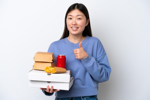Junge Chinesin hält Fast Food isoliert auf weißem Hintergrund und gibt eine Daumen hoch Geste