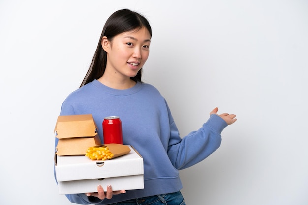 Junge Chinesin hält Fast Food isoliert auf weißem Hintergrund und streckt die Hände zur Seite aus, um zum Kommen einzuladen