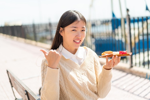 Junge Chinesin hält Sashimi im Freien und zeigt zur Seite, um ein Produkt zu präsentieren