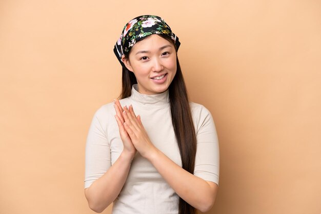 Junge Chinesin isoliert auf beigem Hintergrund applaudiert nach der Präsentation auf einer Konferenz