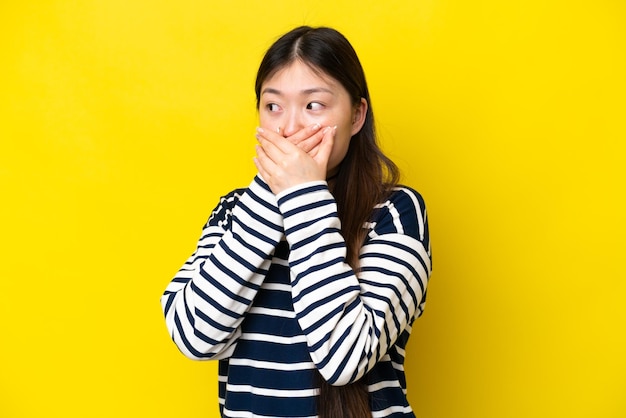 Junge Chinesin isoliert auf gelbem Hintergrund, die den Mund bedeckt und zur Seite schaut