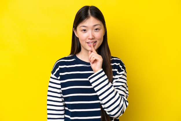 Junge Chinesin isoliert auf gelbem Hintergrund, die ein Zeichen der Stillegeste zeigt, die den Finger in den Mund steckt