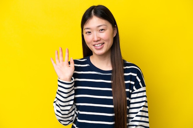 Junge Chinesin isoliert auf gelbem Hintergrund, die mit der Hand mit glücklichem Ausdruck salutiert