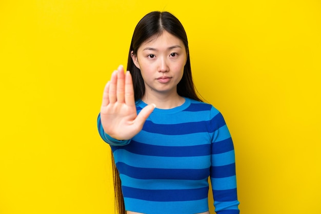 Junge Chinesin isoliert auf gelbem Hintergrund, die Stoppgeste macht