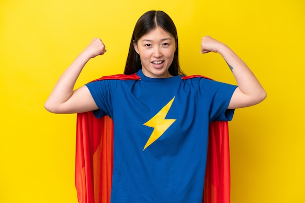 Junge Chinesin isoliert auf gelbem Hintergrund im Superheldenkostüm und mit starker Geste