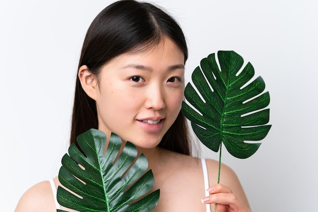 Junge Chinesin isoliert auf weißem Hintergrund, die ein Palmblatt mit glücklichem Ausdruck hält Close up Portrait