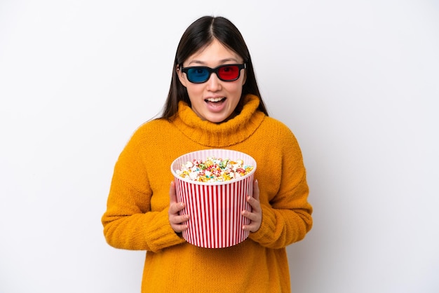 Junge Chinesin isoliert auf weißem Hintergrund mit 3D-Brille und mit einem großen Eimer Popcorn