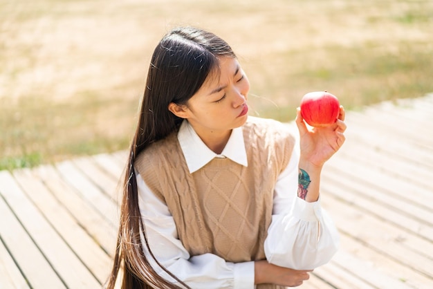 Junge Chinesin mit einem Apfel im Freien mit traurigem Ausdruck