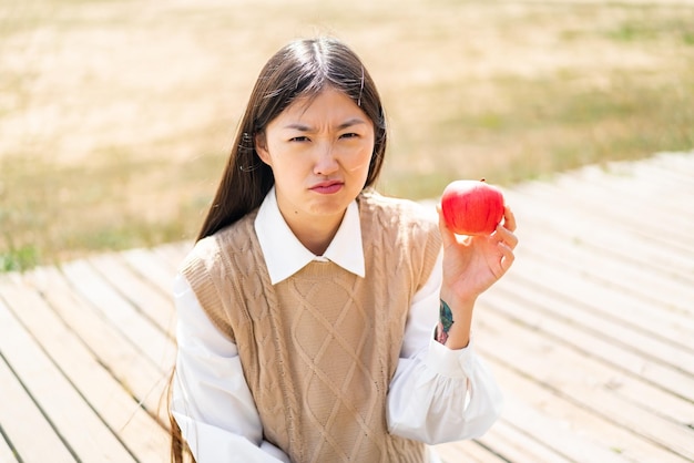 Junge Chinesin mit einem Apfel im Freien mit traurigem Ausdruck