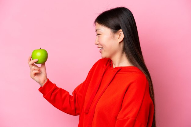 Junge Chinesin mit einem Apfel isoliert auf rosa Hintergrund mit fröhlichem Ausdruck