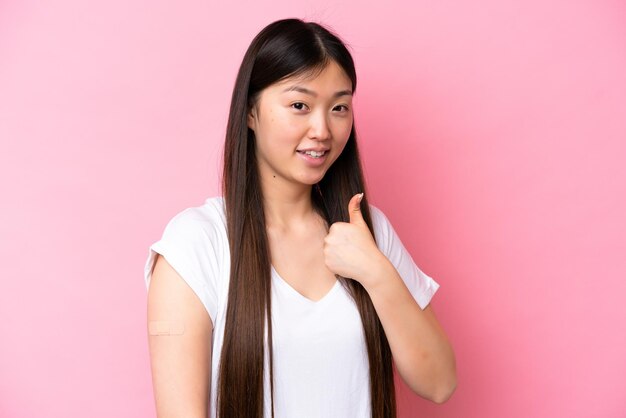 Junge Chinesin trägt ein Pflaster isoliert auf rosa Hintergrund mit Daumen nach oben, weil etwas Gutes passiert ist