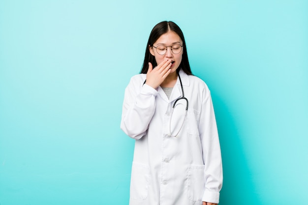 Junge chinesische Doktorfrau, die einen müden Gestenbedeckungsmund mit der Hand zeigend gähnt.