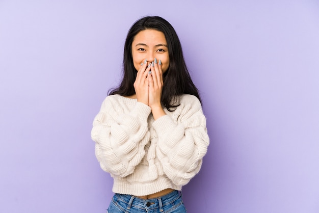 Junge chinesische Frau auf einer lila Wand, die über etwas lacht und Mund mit Händen bedeckt.