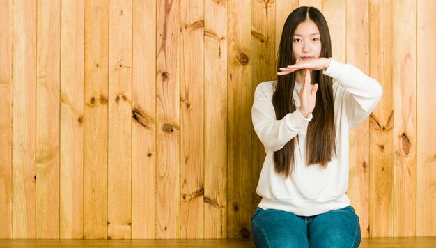 Foto junge chinesische frau, die auf einem hölzernen platz sitzt, der eine auszeitgeste zeigt.