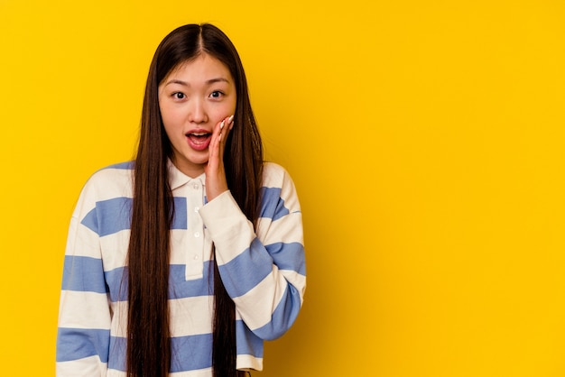 Junge chinesische Frau, die auf gelbem Hintergrund isoliert wird, schreit laut, hält Augen offen und Hände angespannt.