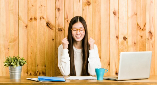 Junge chinesische Frau, die auf ihrem Schreibtisch anhebt Faust studiert, glücklich und erfolgreich sich fühlt.