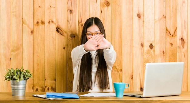 Junge chinesische Frau, die auf ihrem Schreibtisch tut eine Ablehnungsgeste studiert