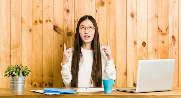 Junge chinesische Frau, die auf ihrem Schreibtisch zeigt Oberseite mit geöffnetem Mund studiert.