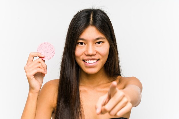 Junge chinesische Frau, die ein fröhliches Lächeln einer Gesichtsscheibe hält, zeigt nach vorne.