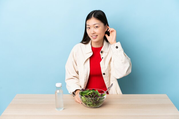 Junge chinesische Frau, die einen lachenden Salat isst