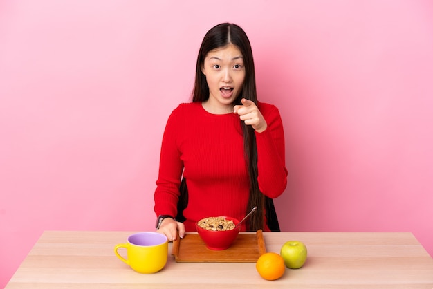 Junge chinesische Frau, die Frühstück in einem Tisch überrascht und nach vorne zeigt