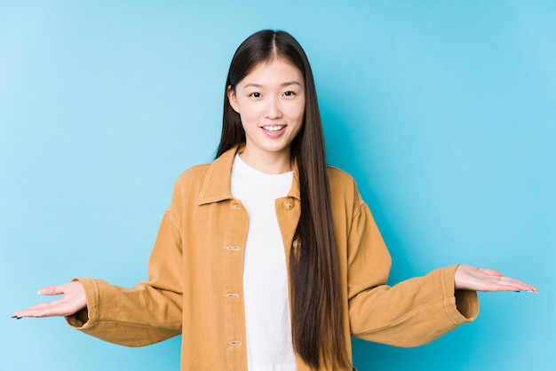 Junge chinesische Frau, die in einer blauen Wand aufwirft, die einen willkommenen Ausdruck zeigt.