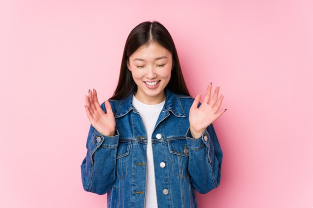 Junge chinesische Frau, die in einer rosa Wand freudig viel lachend posiert