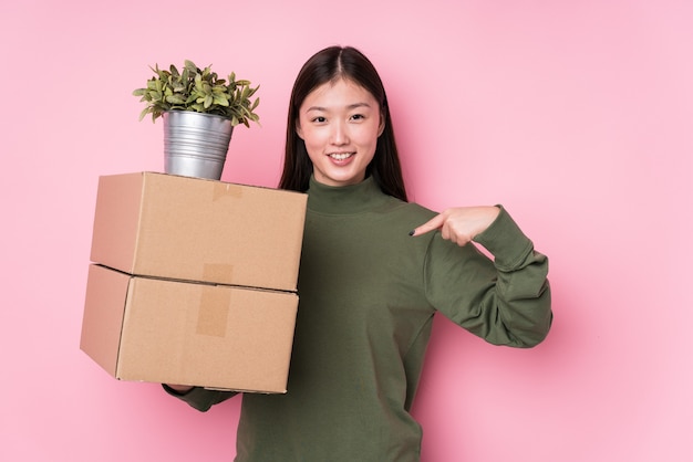 Junge chinesische Frau, die isolierte Personen der Kisten hält, die von Hand auf einen Hemdkopierraum zeigen, stolz und zuversichtlich