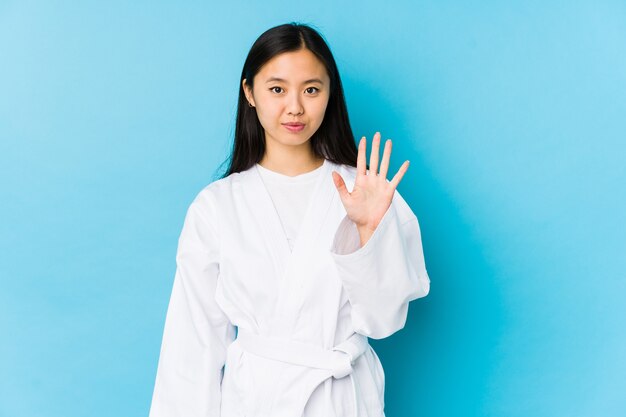 Junge chinesische Frau, die Karate praktiziert, lächelnd fröhlich lächelnd zeigt Nummer fünf mit den Fingern.