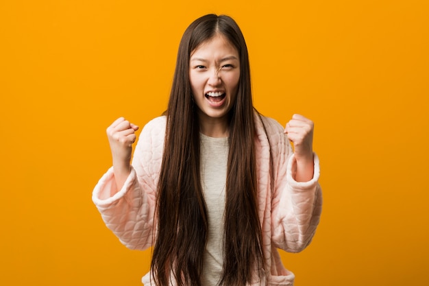 Junge chinesische Frau im Pyjama sorglos und aufgeregt zujubeln. Sieg-Konzept.