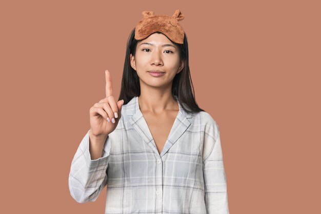 Junge chinesische Frau in Schlafanzugmaske zeigt Nummer eins mit dem Finger