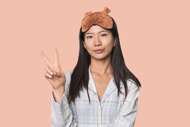 Junge chinesische Frau in Schlafanzugmaske zeigt Nummer zwei mit Fingern