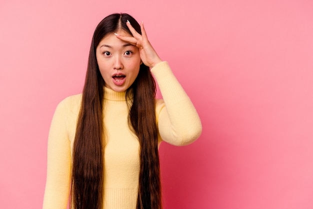 Junge chinesische Frau isoliert auf rosa Hintergrund schreit laut, hält Augen geöffnet und Hände angespannt.