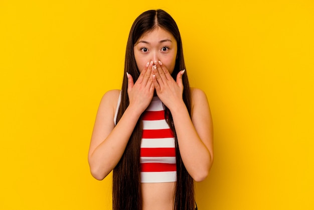 Junge chinesische Frau lokalisiert auf gelbem Hintergrund schockiert, Mund mit Händen bedeckend.