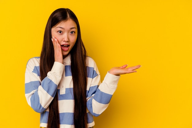 Junge chinesische Frau lokalisiert auf gelber Wand beeindruckte das Halten des Kopienraums auf Handfläche.