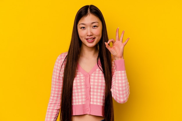Junge chinesische Frau lokalisiert auf gelber Wand fröhlich und zuversichtlich, ok Geste zeigend.