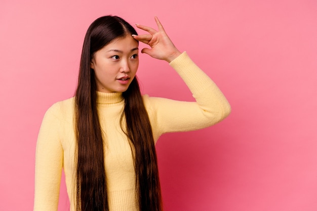 Junge chinesische Frau lokalisiert auf rosa, die weit weg schaut und Hand auf Stirn hält.