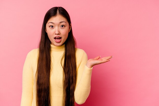 Junge chinesische Frau lokalisiert auf rosa Hintergrund beeindruckte das Halten des Kopienraums auf Handfläche.