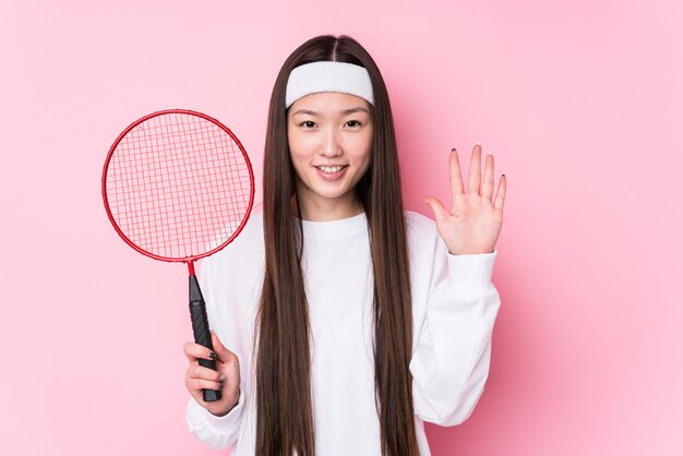 Junge chinesische Frau spielt Badminton lächelnd fröhlich und zeigt Nummer fünf mit den Fingern.